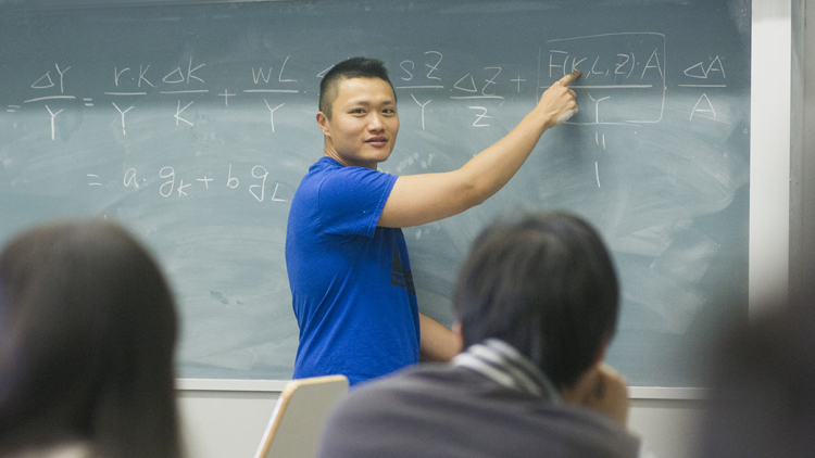 Professor is teaching class and writing on chalkboard