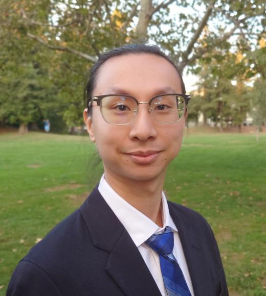 Image of Justin Ku from shoulders up in a park wearing a suit and blue tie