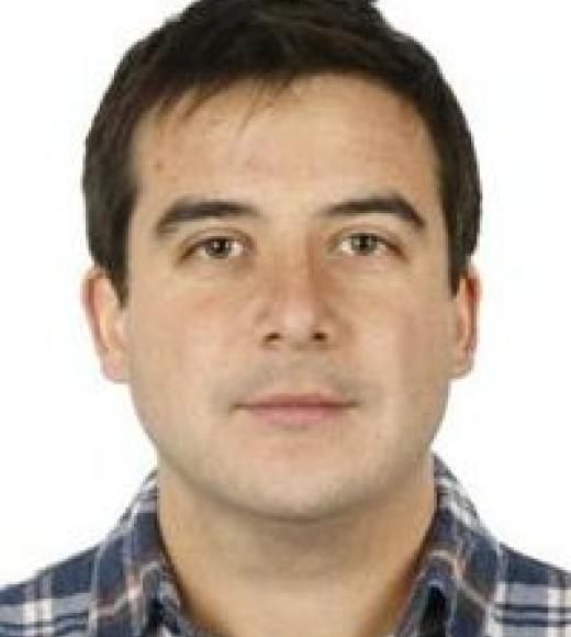 Headshot of young man with short dark hair, plaid shirt, neutral expression, white background.