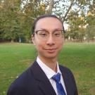 Image of Justin Ku from shoulders up in a park wearing a suit and blue tie