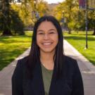 Outdoor headshot — smiling young woman in blazer on sunlit campus path